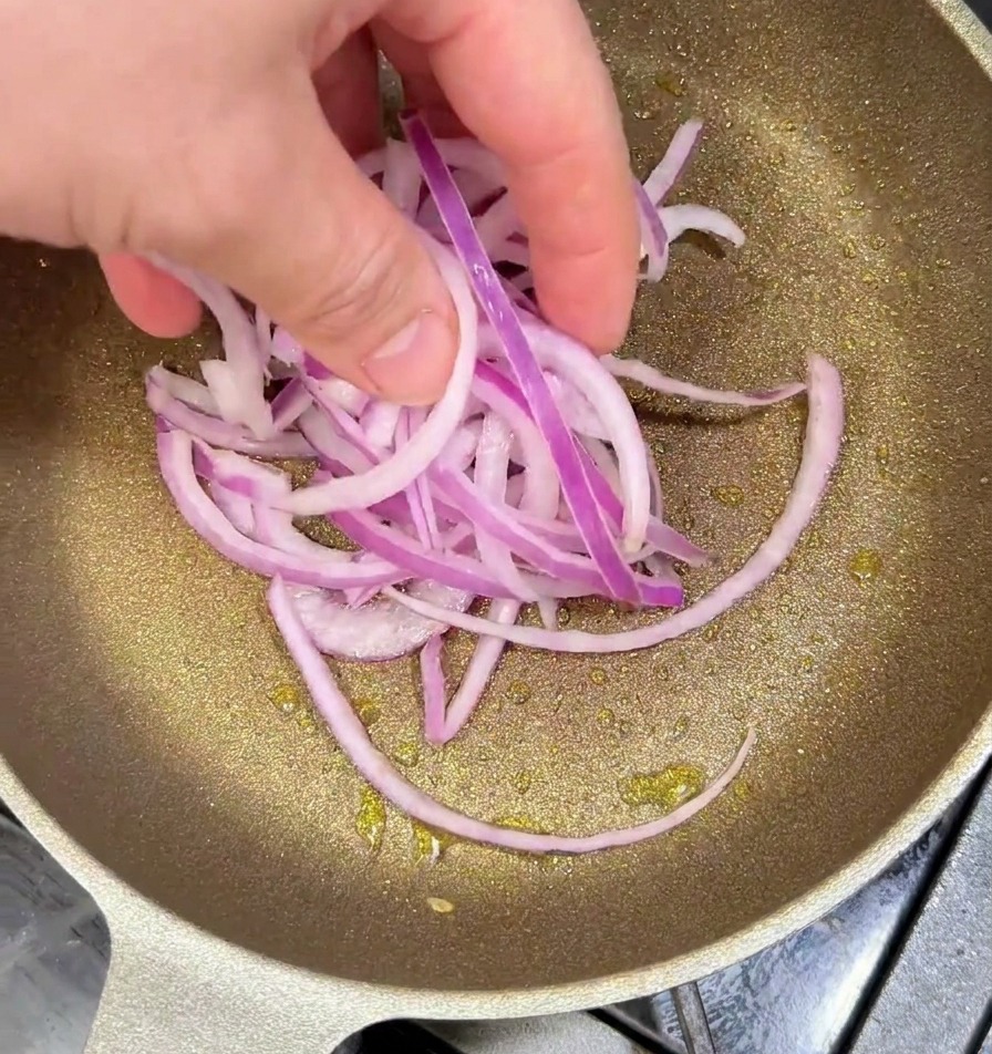 Cipolle rosse affettate aggiunte in una padella calda con olio.