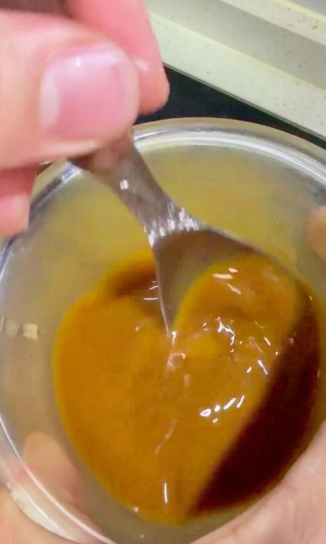 Mano che versa la salsa teriyaki dorata da una ciotola sulla carne e cipolle in padella.