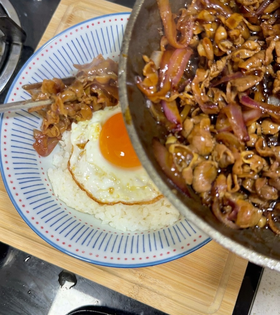 Manzo teriyaki e cipolle versati dalla padella nella ciotola di riso sopra luovo.