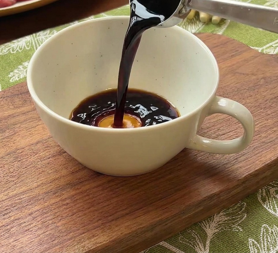 Un cucchiaio di metallo versa salsa di soia scura in una ciotolina bianca con acqua e pasta di peperoncino coreana.