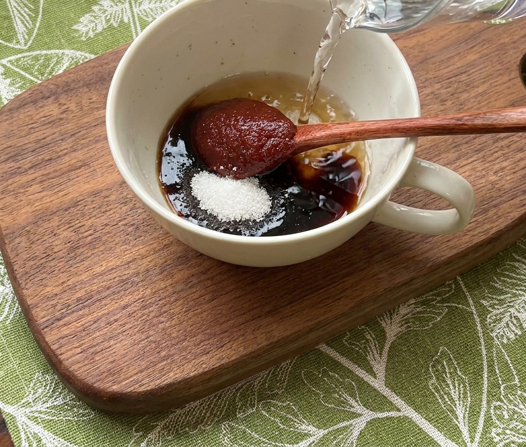 Acqua versata da una caraffa in una ciotola con gli ingredienti della salsa e il Gochujang.