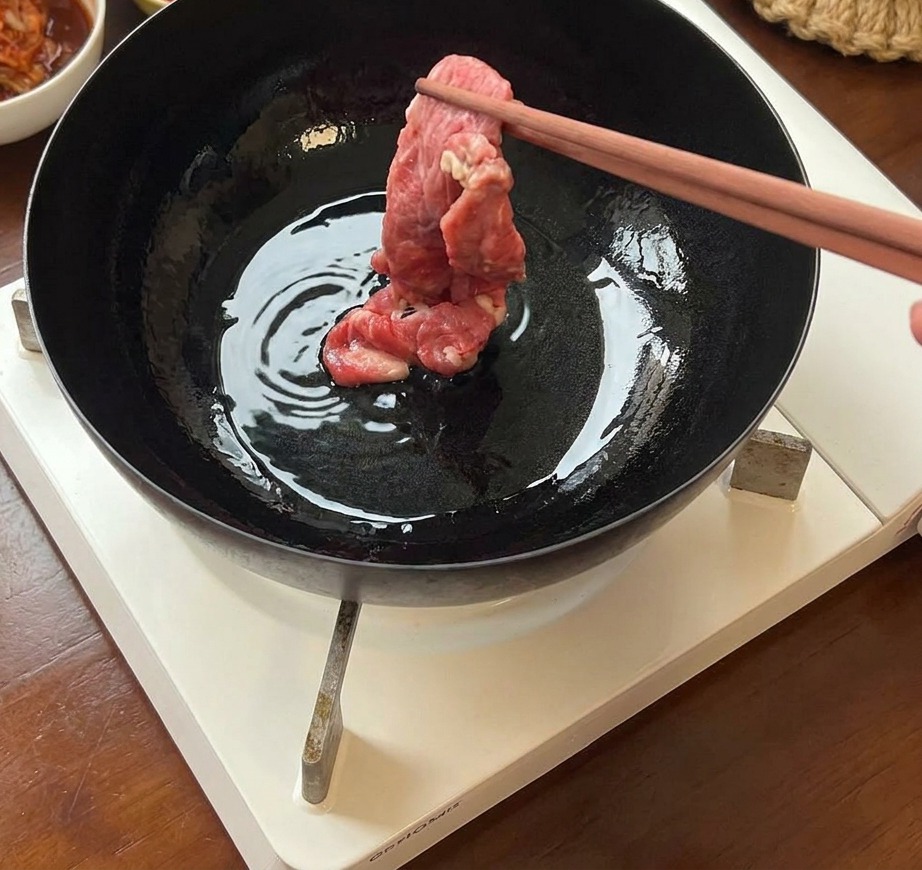 Sottili fette di manzo crudo inserite in una padella di ferro calda e oliata usando delle bacchette.