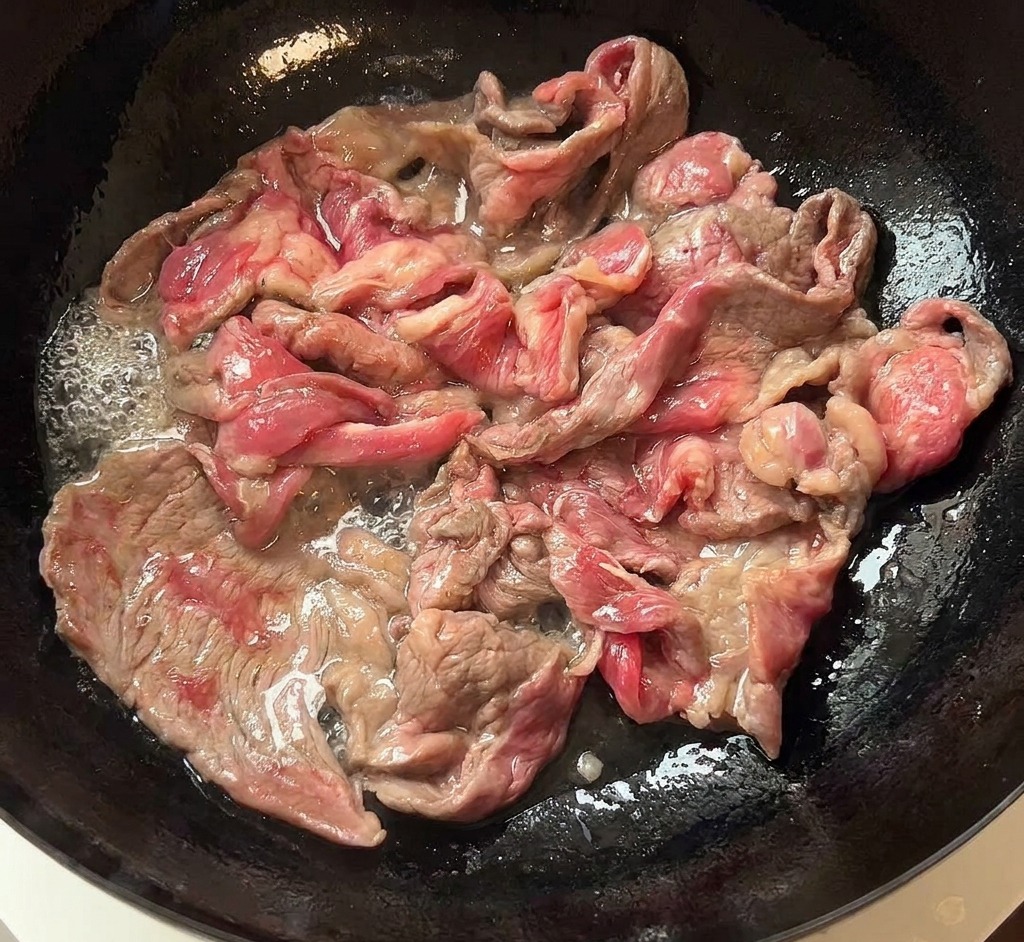 Fettine di manzo rosolate spostate dalla padella a un piatto di ceramica bianca.