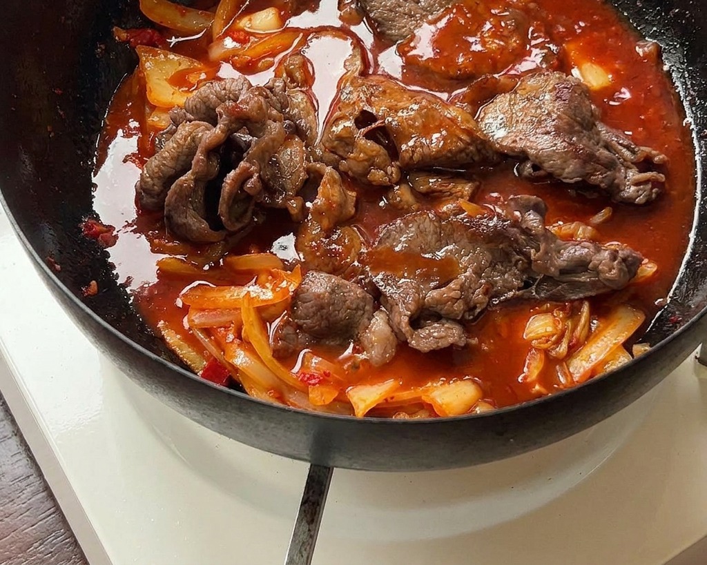 Il mix di manzo e kimchi sobbolle in una salsa rossa densa allinterno di una padella di ferro.