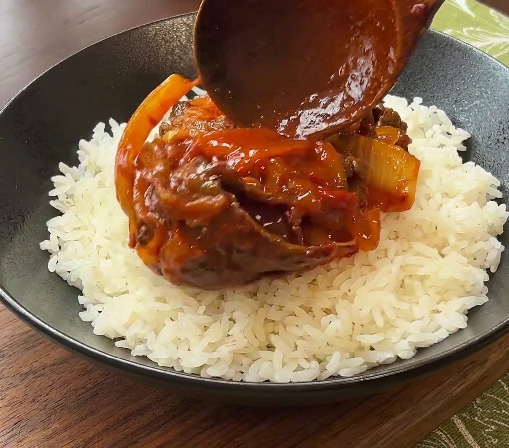 Un cucchiaio di legno adagia il manzo al kimchi sul riso bianco in una ciotola scura.