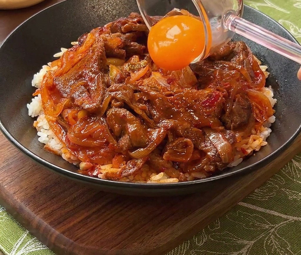Un tuorlo duovo arancione posizionato sulla ciotola di manzo e riso.