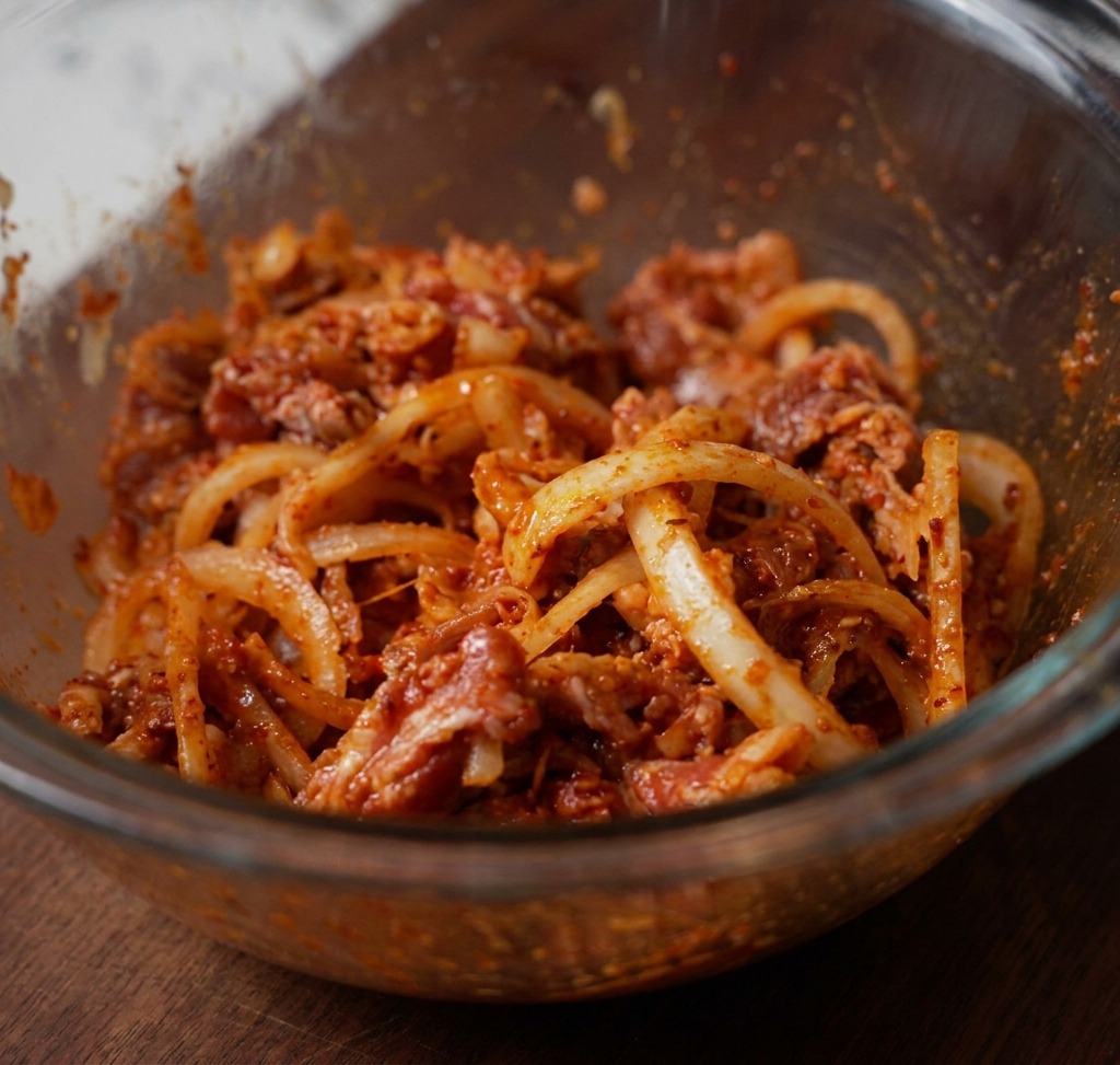 Fettine di manzo, cipolle bianche e pasta di peperoncino mescolate accuratamente in una ciotola di vetro, pronte per la marinatura.