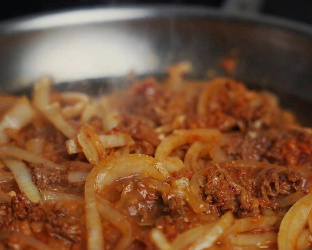 Acqua aggiunta a una padella con manzo e cipolle saltate, creando una salsa ribollente.