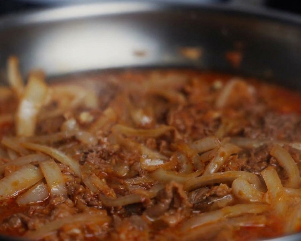 Dettaglio di pepe nero e salsa di soia aggiunti a una padella di manzo e cipolle che sobbolle.