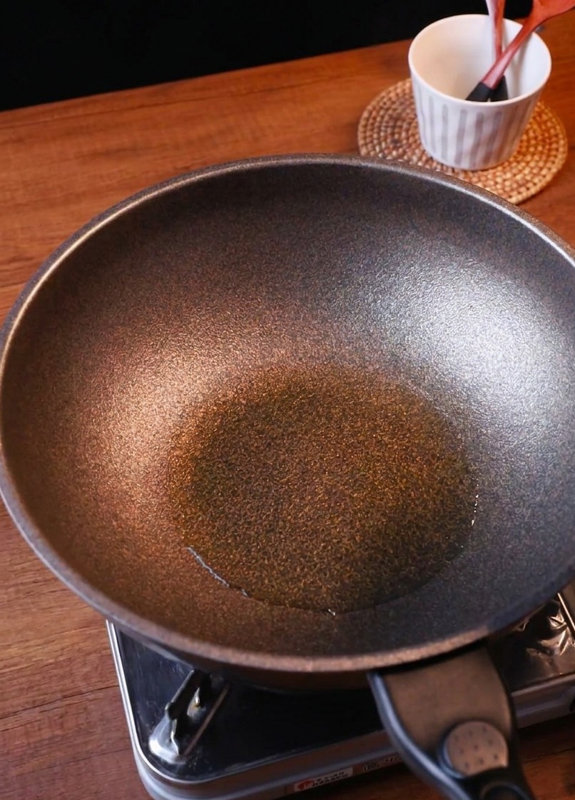 Cipolle appena affettate e una porzione di kimchi tritato versati in una padella insaporita.