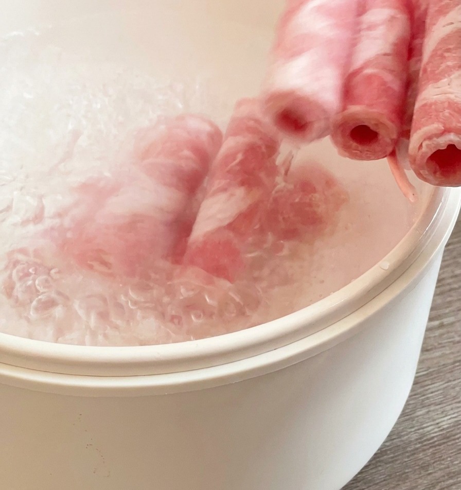 Sottili fette di manzo immerse in una pentola bianca con acqua bollente per una rapida cottura.