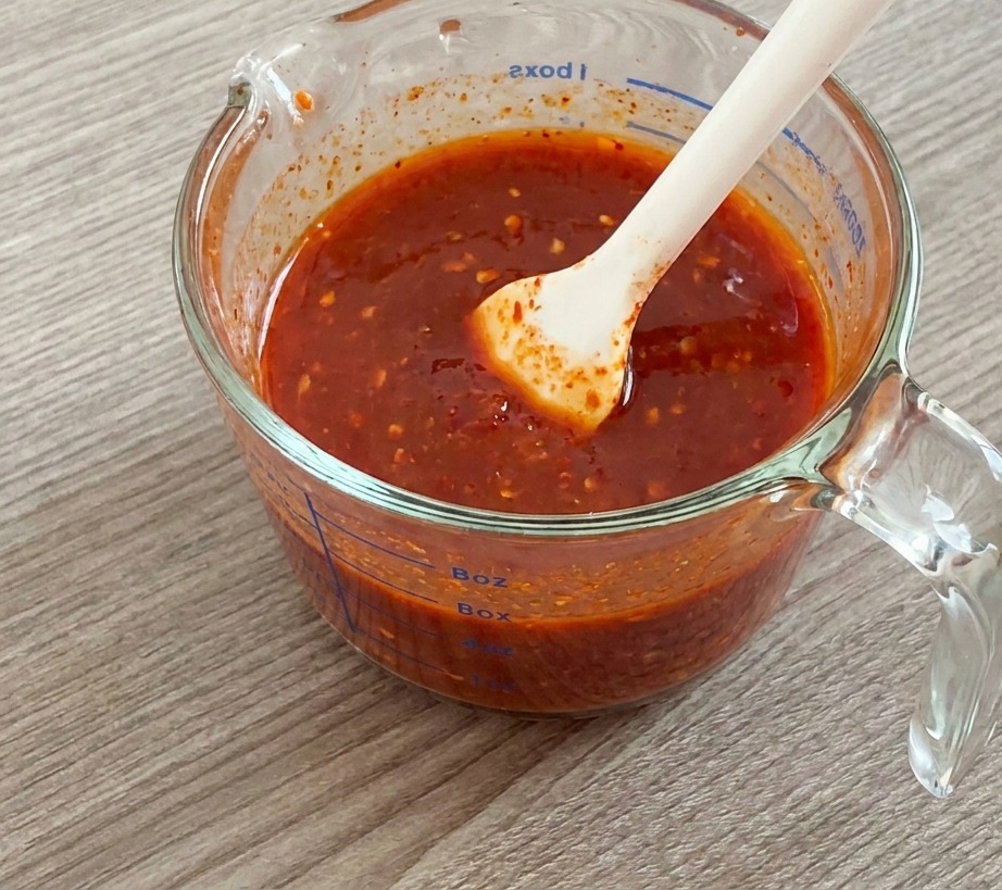 Una spatola in silicone bianco che mescola una salsa rosso brillante allinterno di un misurino di vetro.