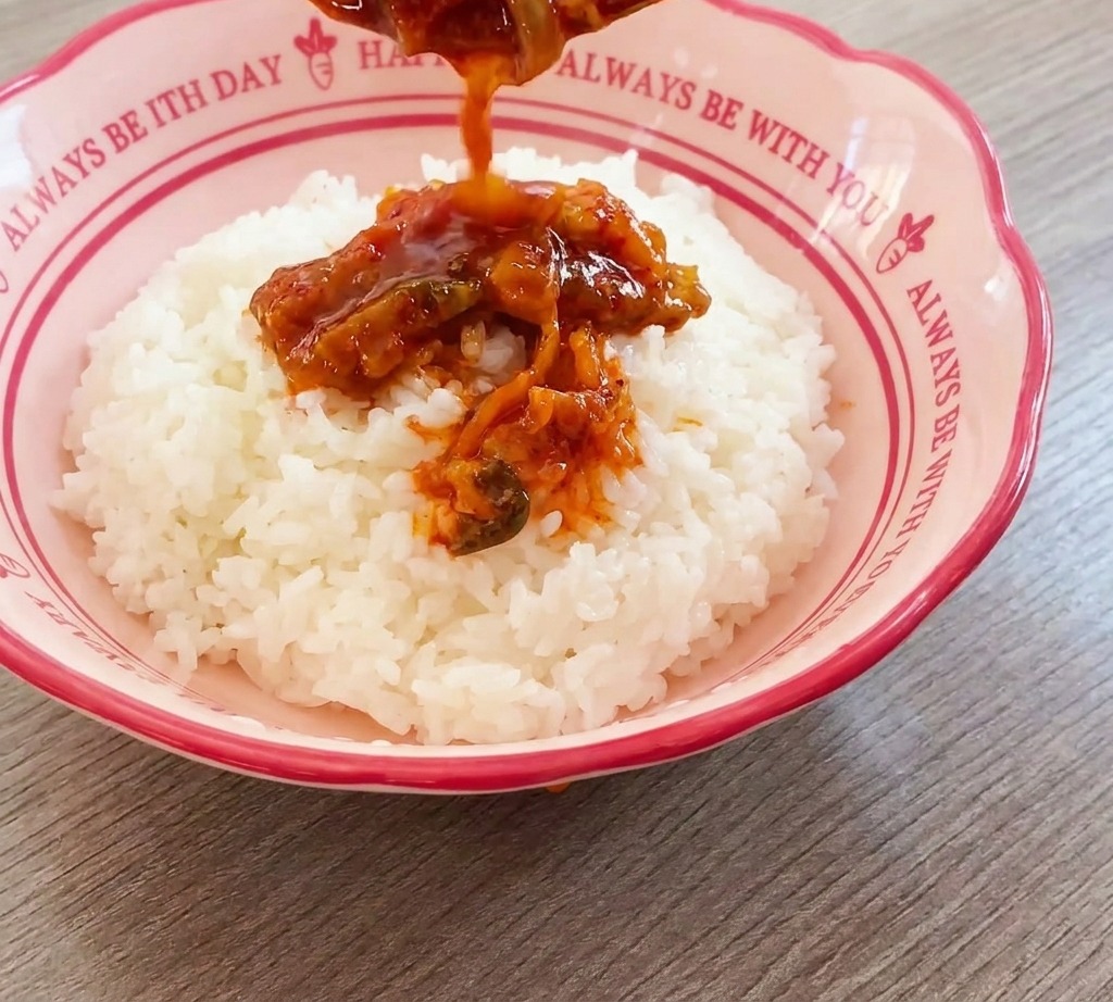 Il mix di manzo e kimchi versato da un cucchiaio sopra una base di riso bianco in una ciotola rosa.