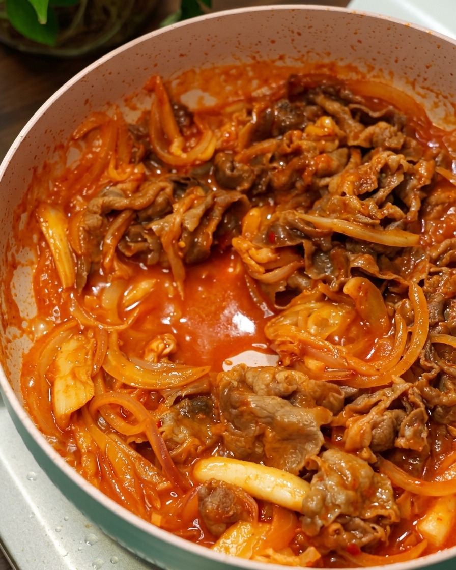 Manzo e cipolle che saltano in una densa salsa rossa coreana in una padella rosa.