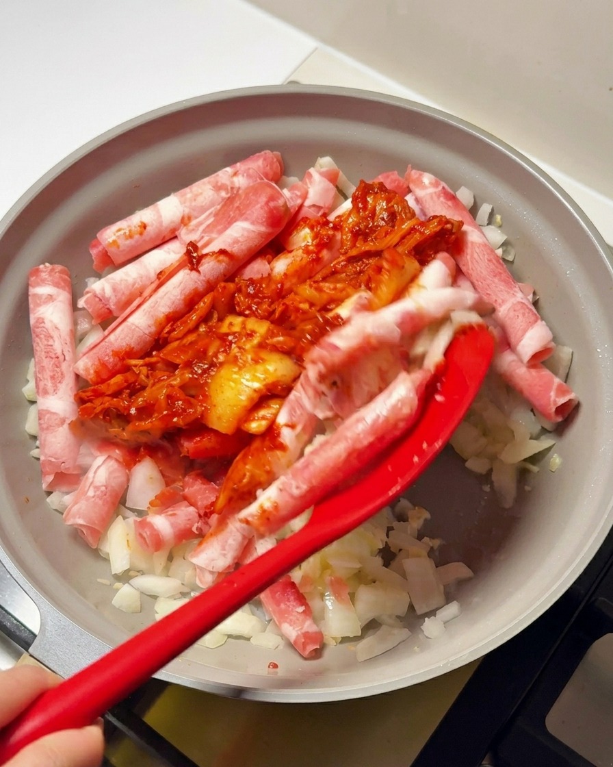 Una spatola rossa mescola una salsa densa a base di kimchi e peperoncino con la carne e le cipolle nella padella.