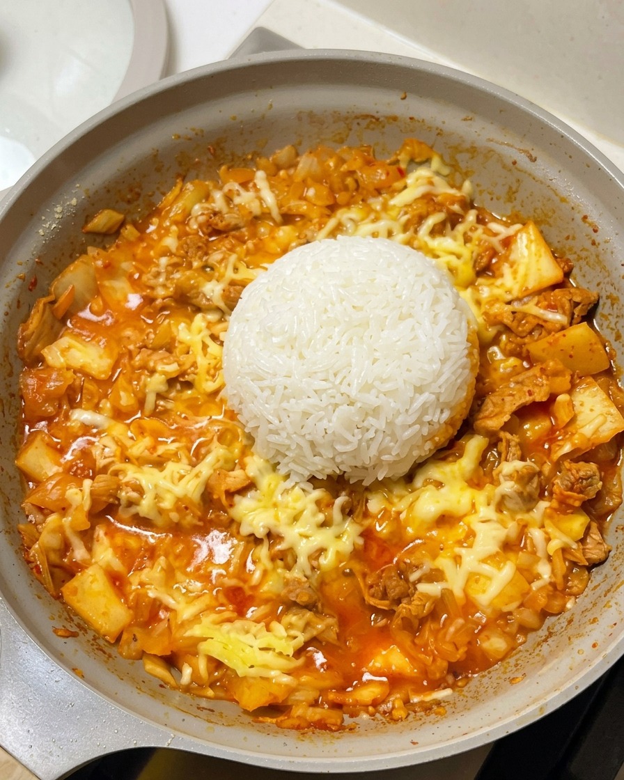 Una cupola perfetta di riso bianco cotto posizionata al centro della padella, circondata dal formaggio fuso e dalla base rossa di carne e kimchi.