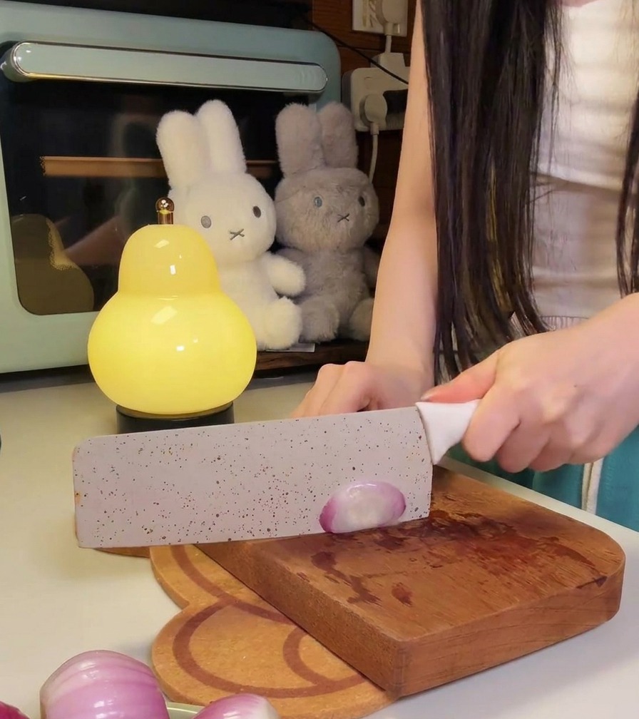 Una persona che usa un coltello da cucina per affettare finemente delle cipolle rosse su un tagliere di legno.