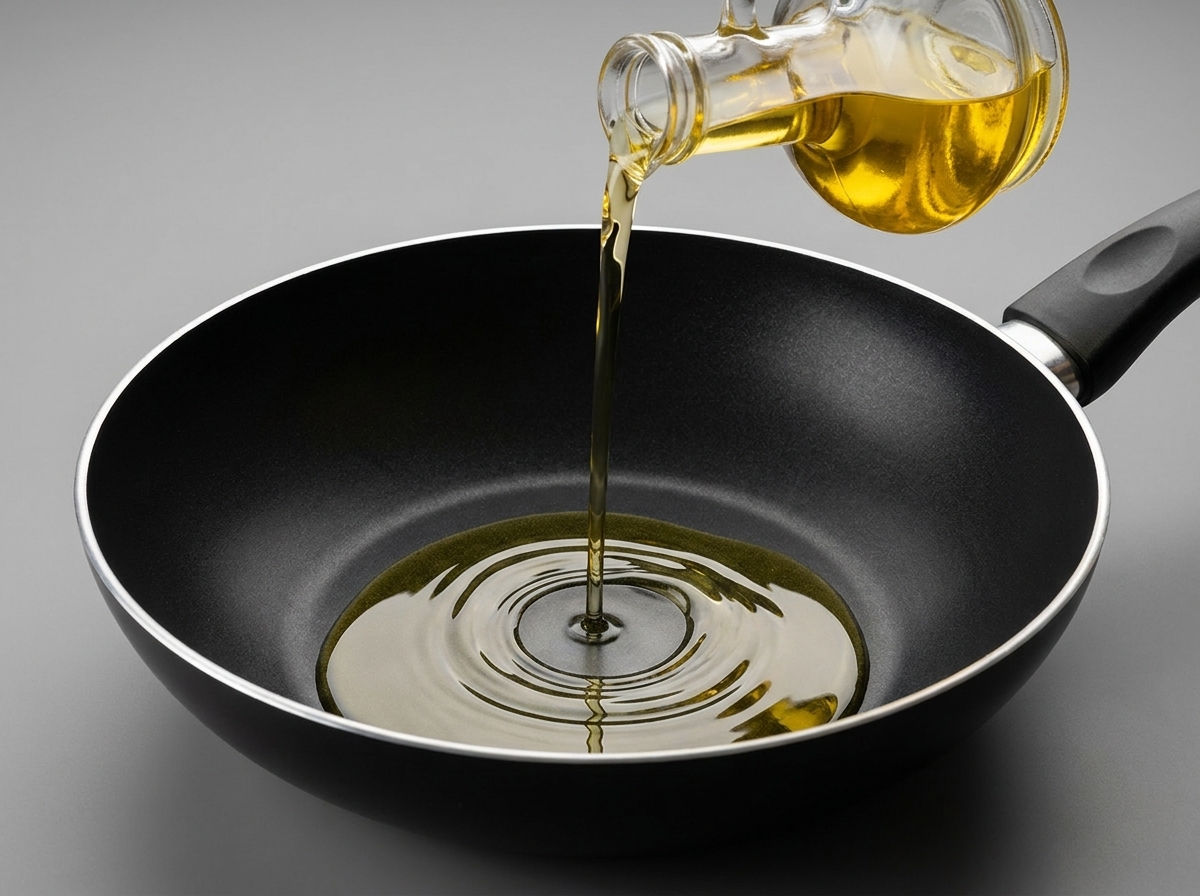 Olio di semi versato da una bottiglia di vetro in un wok nero antiaderente pulito.