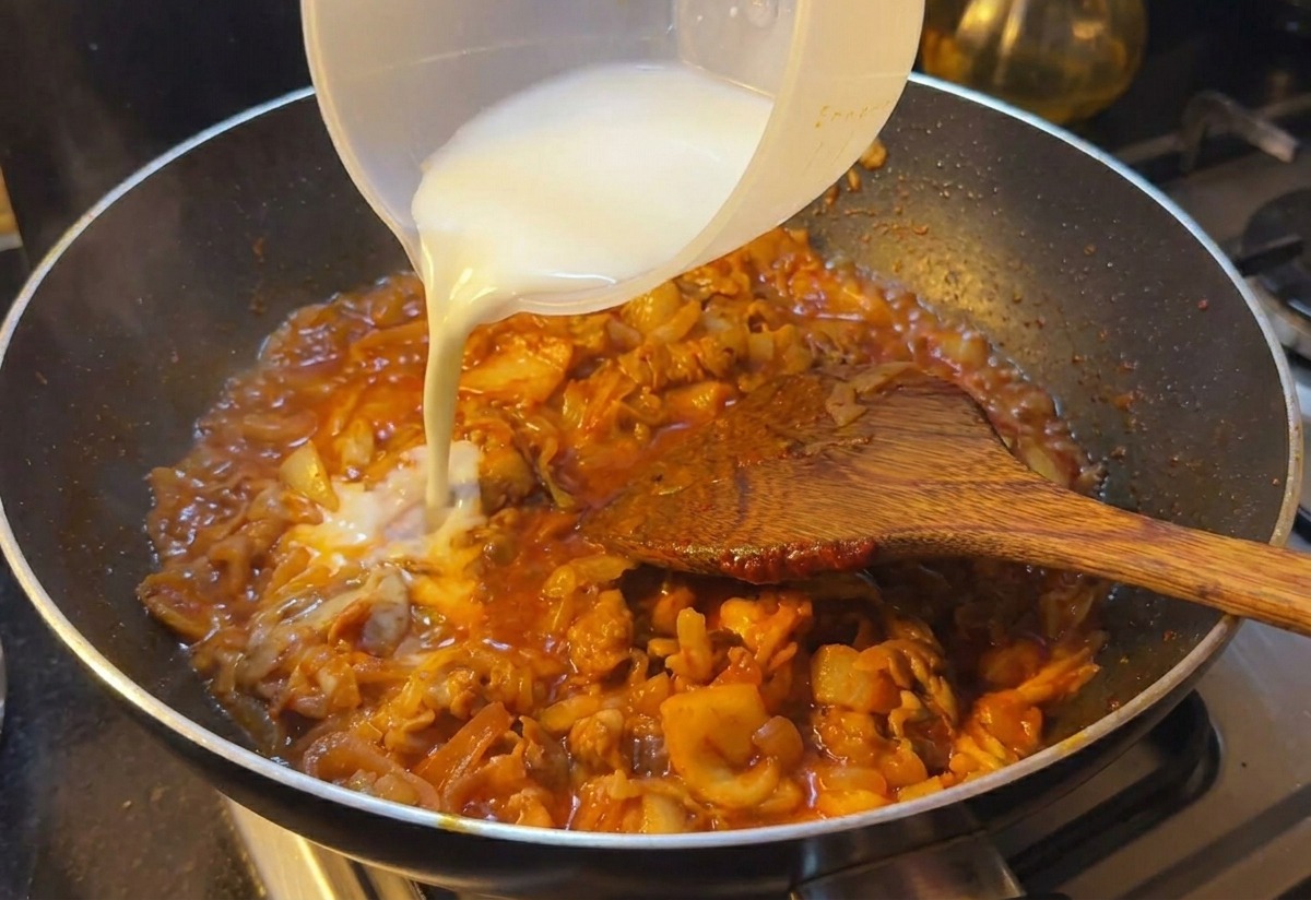 Acqua con amido versata da un contenitore di plastica in una padella con manzo e kimchi in una ricca salsa rossa.