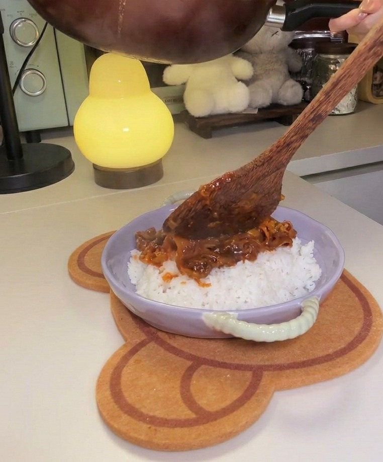 Padella inclinata per versare il mix di manzo e kimchi su un letto di riso bianco in una ciotola color lavanda.
