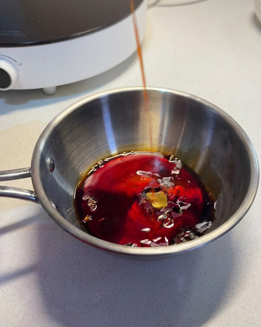 Un liquido scuro e saporito versato in una ciotola di acciaio inox che contiene gli altri ingredienti della salsa.