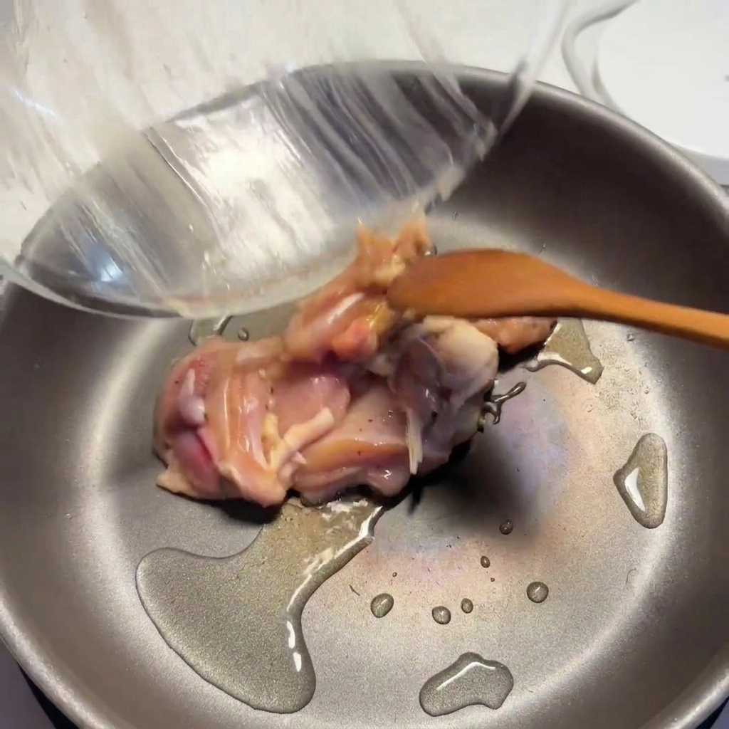 Pezzi di pollo conditi che cuociono in una padella calda con olio, con la superficie che inizia a dorarsi.