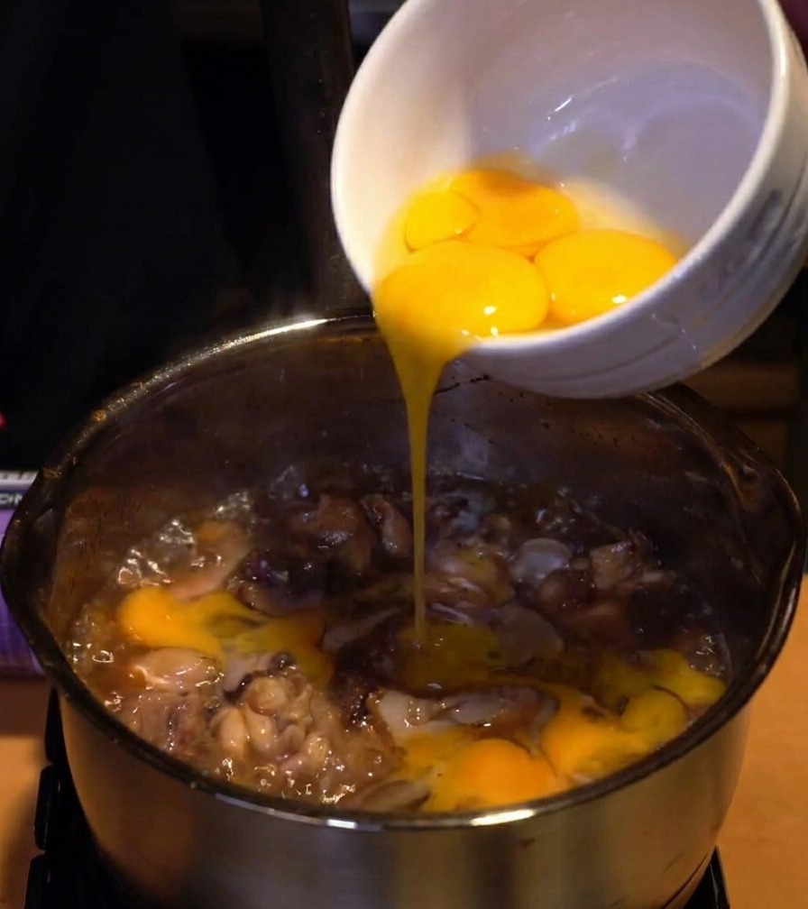 Albumi duovo versati da una ciotola di ceramica bianca in un pentolino di pollo e cipolle che sobbollono.