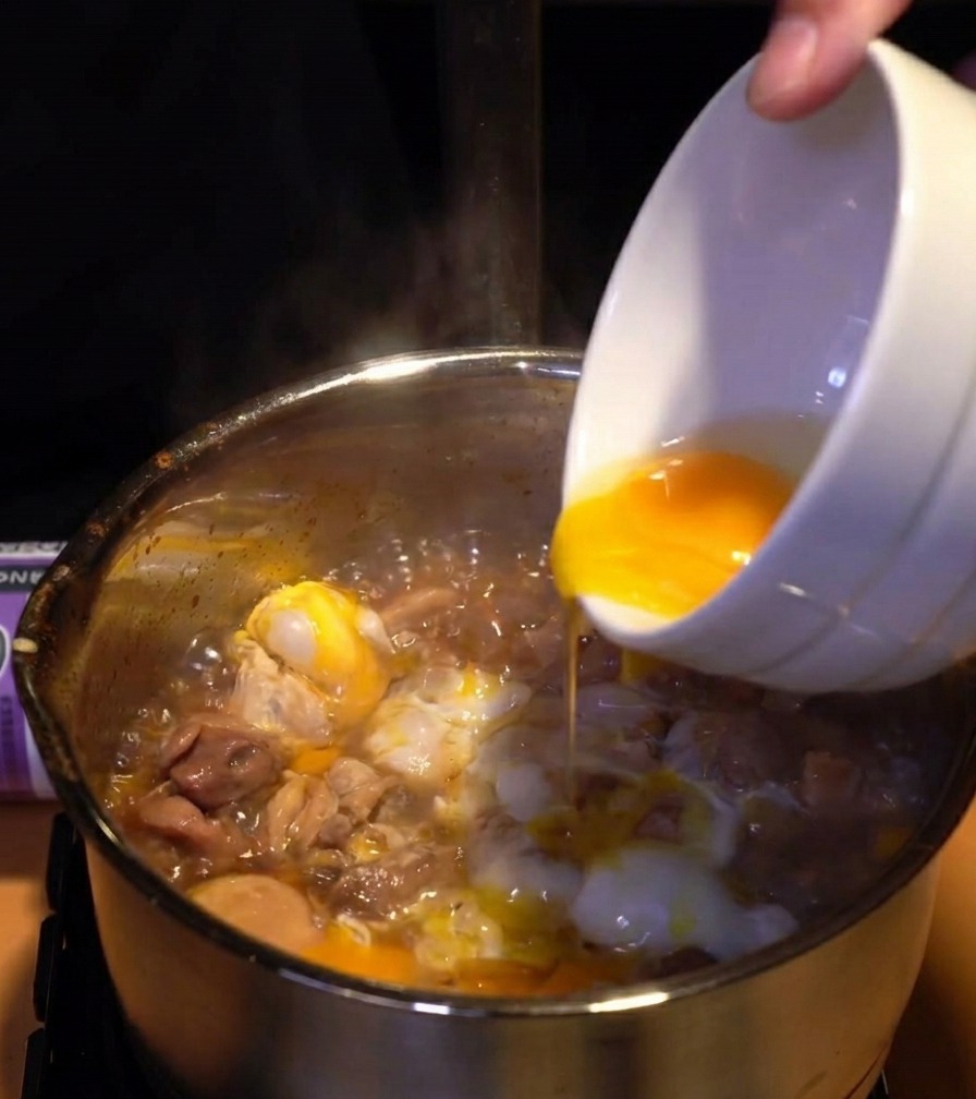 Tuorli duovo giallo brillante versati da una ciotola sopra uno strato di albumi cotti e pollo in un pentolino.