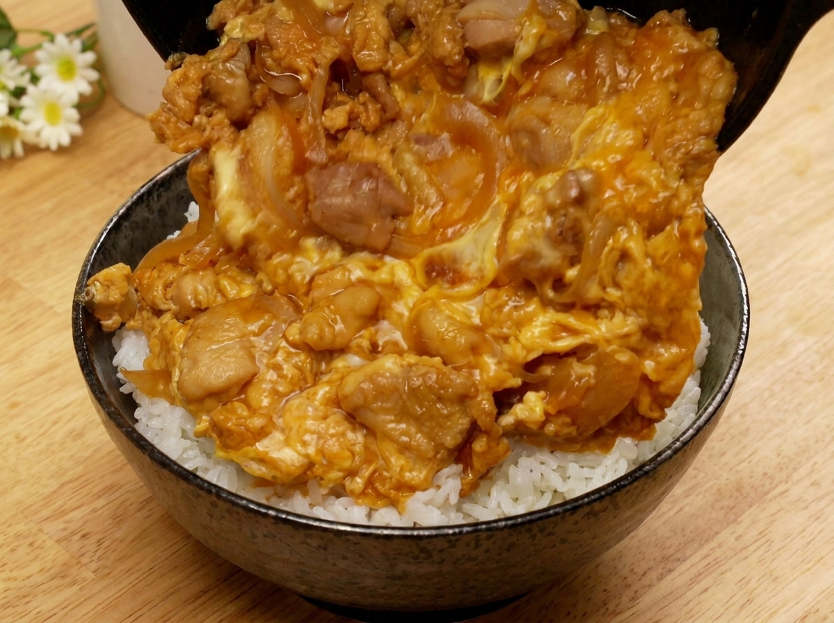 Una padella inclinata per far scivolare il condimento di Oyakodon su una ciotola di riso bianco.