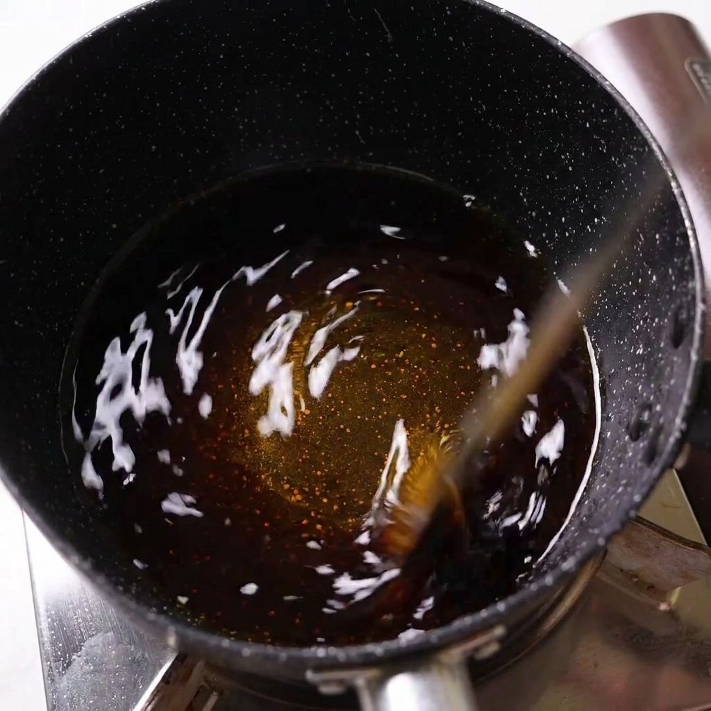 Liquido scuro di condimento mescolato in un pentolino nero su un fornello.