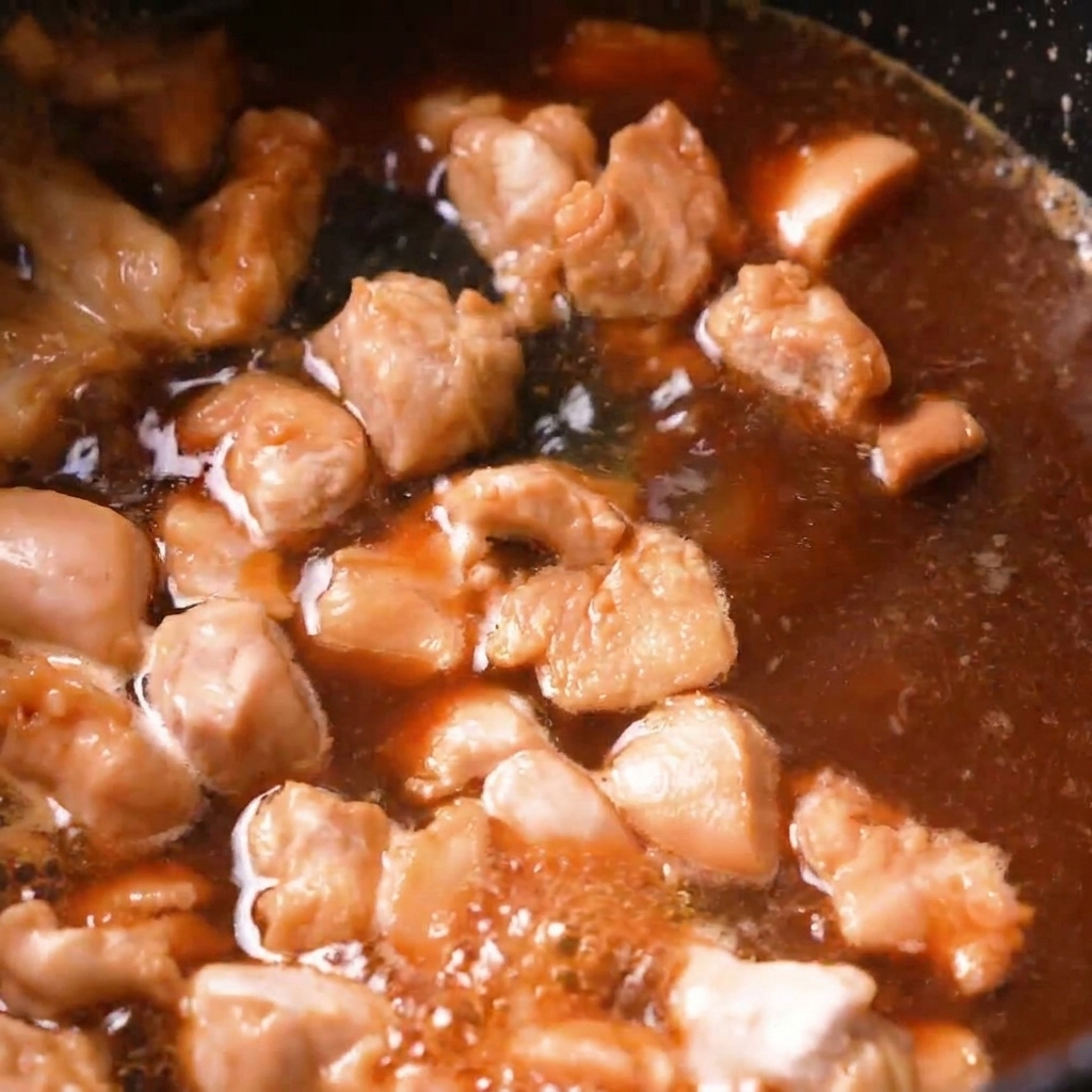 Pezzi di pollo che sobbollono in un brodo dashi marrone allinterno di una padella scura.