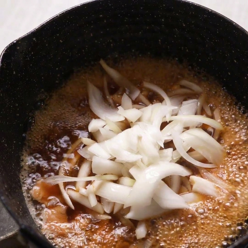 Cipolle crude affettate sottilmente aggiunte a una padella con pollo e brodo dashi.