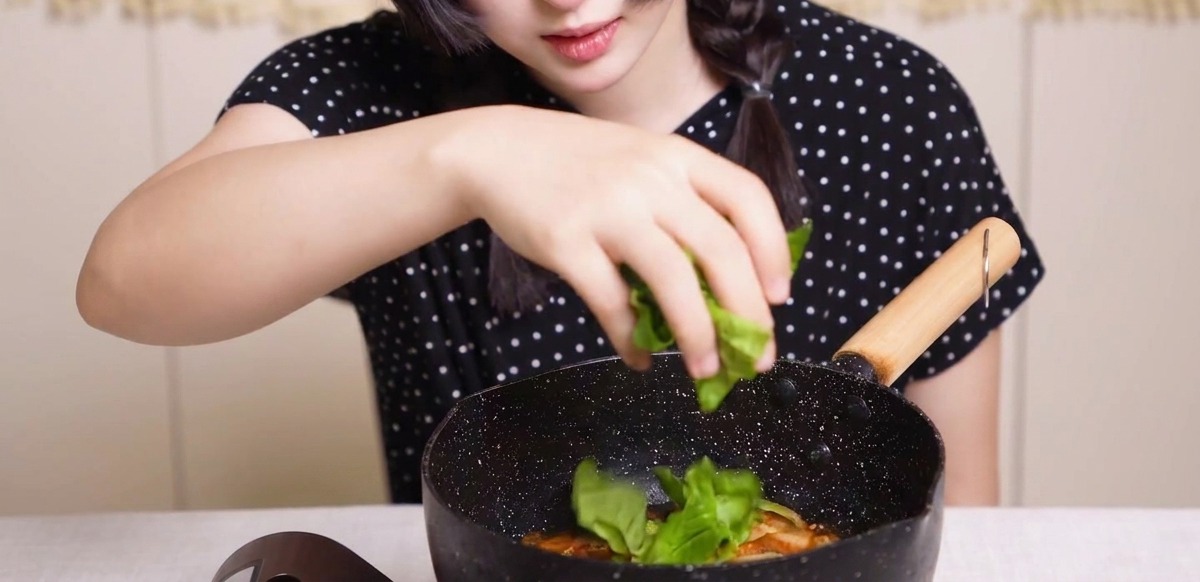 Verdure verdi fresche distribuite a mano in una padella con pollo, cipolle e uova in salsa dashi.