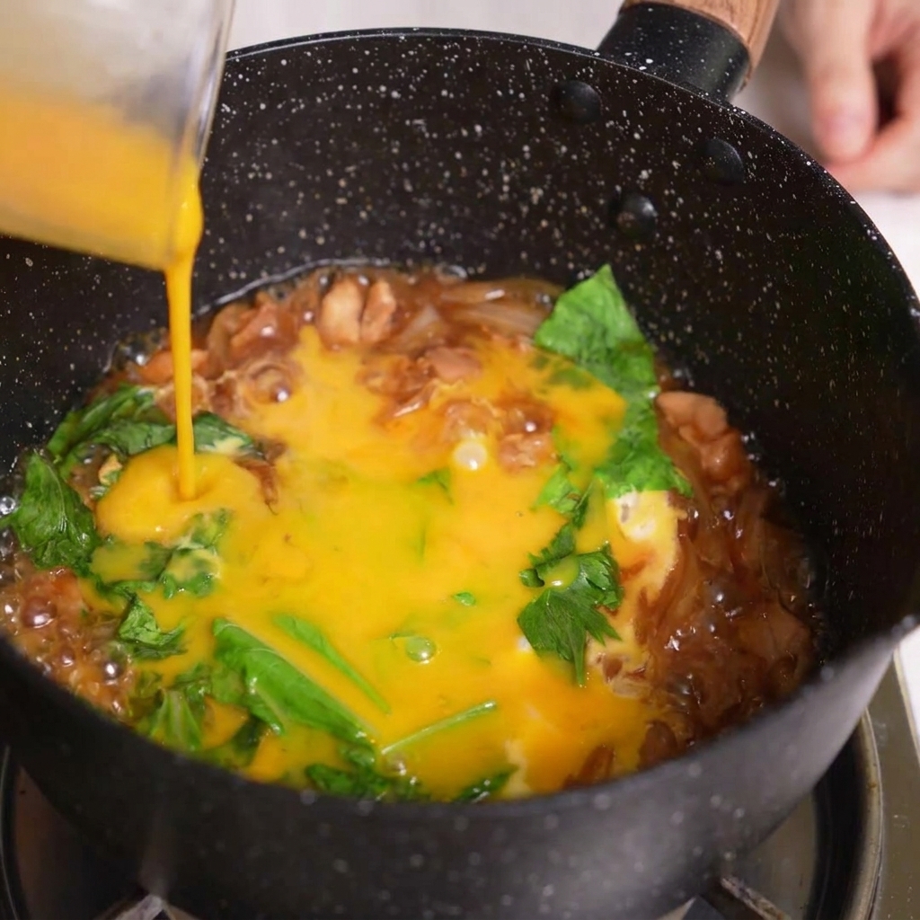 Versare lultima parte di uovo sbattuto sopra gli ingredienti dellOyakodon in padella.
