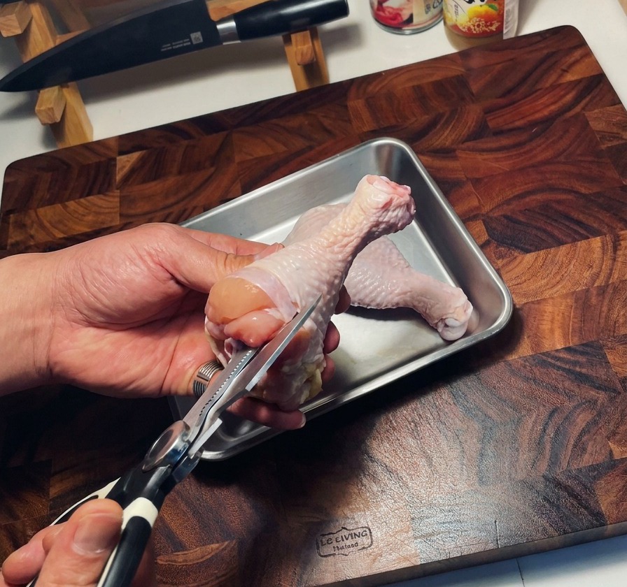 Delle forbici da cucina che rimuovono losso da una sovracoscia di pollo cruda su un vassoio di metallo.