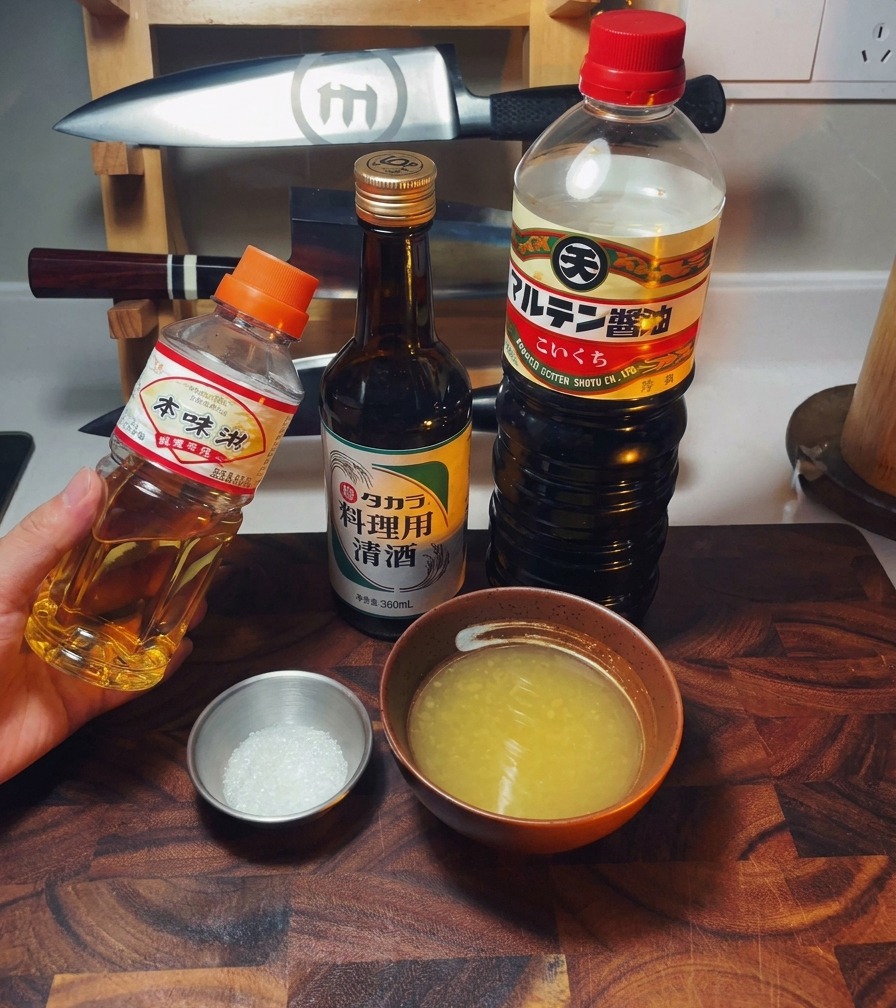 Bottiglie di mirin, sake e salsa di soia accanto a una ciotola di brodo di pollo e zucchero.