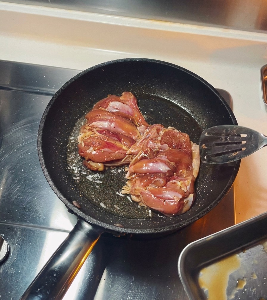Due sovracosce di pollo condite che friggono con la pelle rivolta verso il basso in una padella nera.