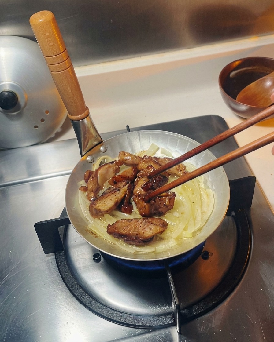 Pezzi di pollo fritto adagiati su un letto di cipolle soffritte traslucide in una piccola padella dargento.