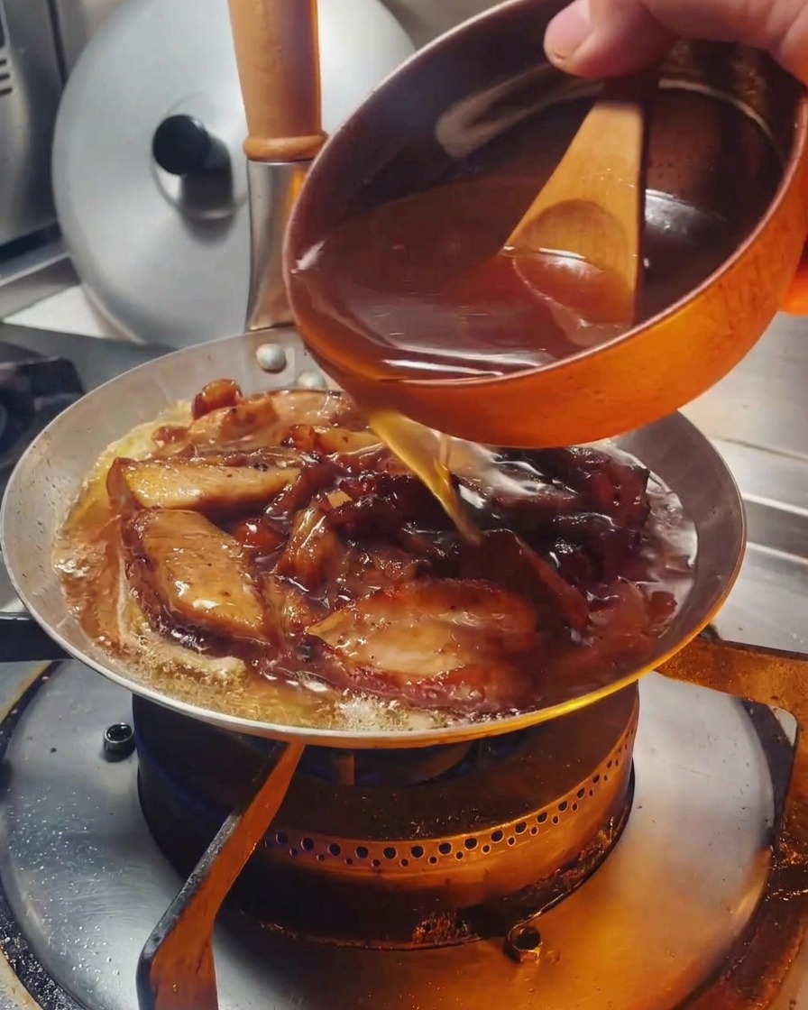 Una salsa marrone versata da una ciotolina in una padella contenente pollo e cipolle.