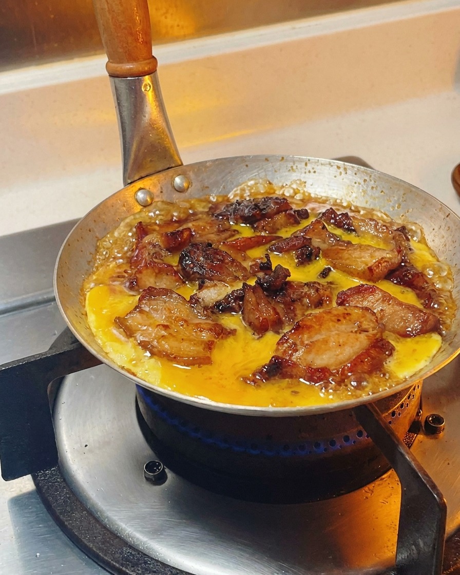 Composto di uova sbattute versato con un movimento circolare sopra pollo e cipolle che sobbollono nella salsa.