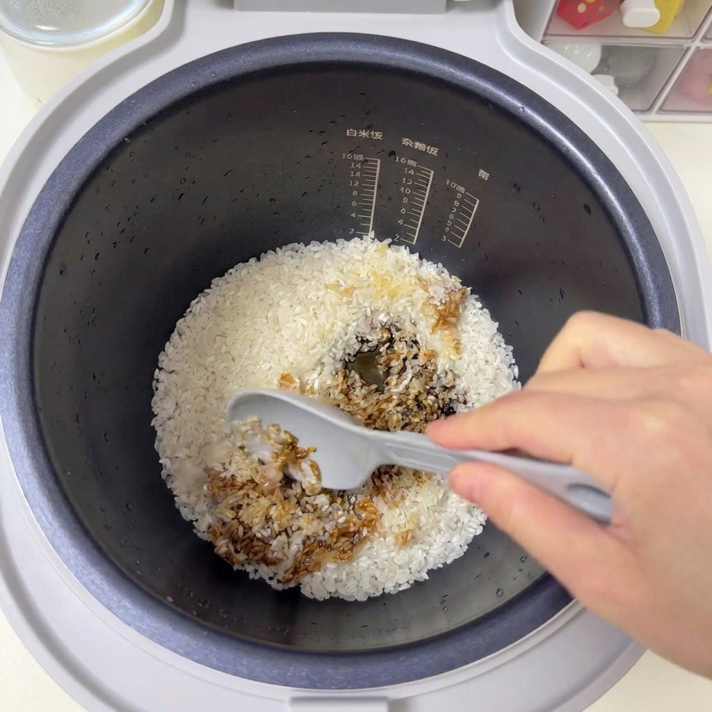 Una spatola grigia mescola il riso bianco e le salse scure allinterno della pentola del cuociriso.
