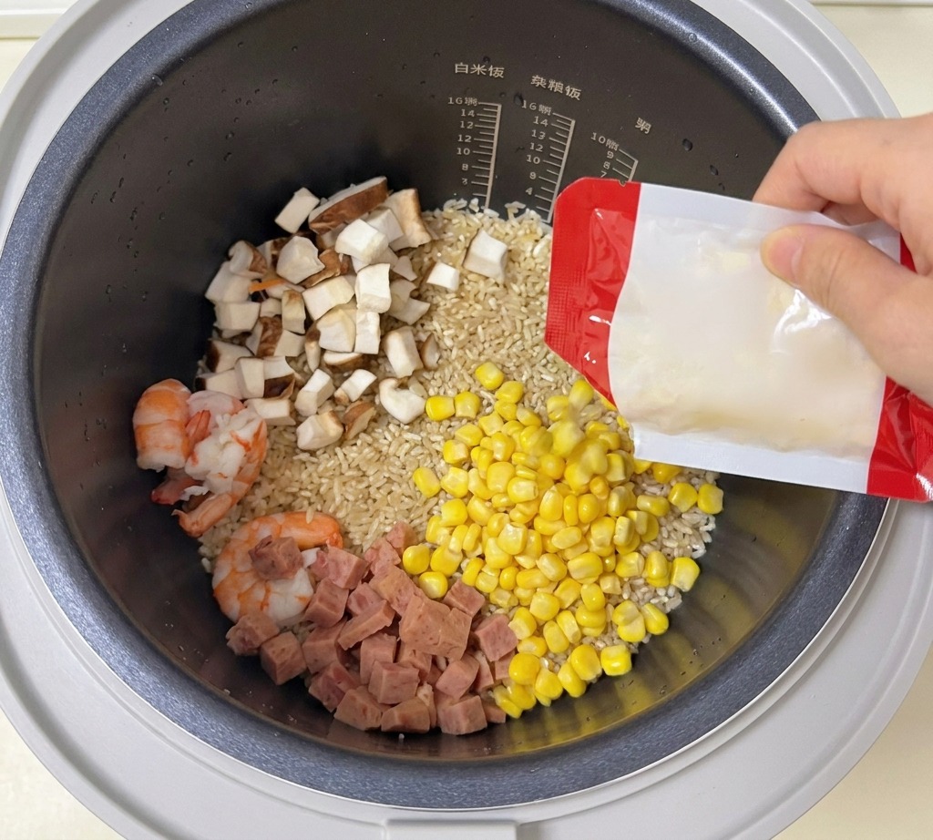 Chicchi di mais dolce versati da una confezione in un cuociriso contenente riso, gamberi, funghi e carne.