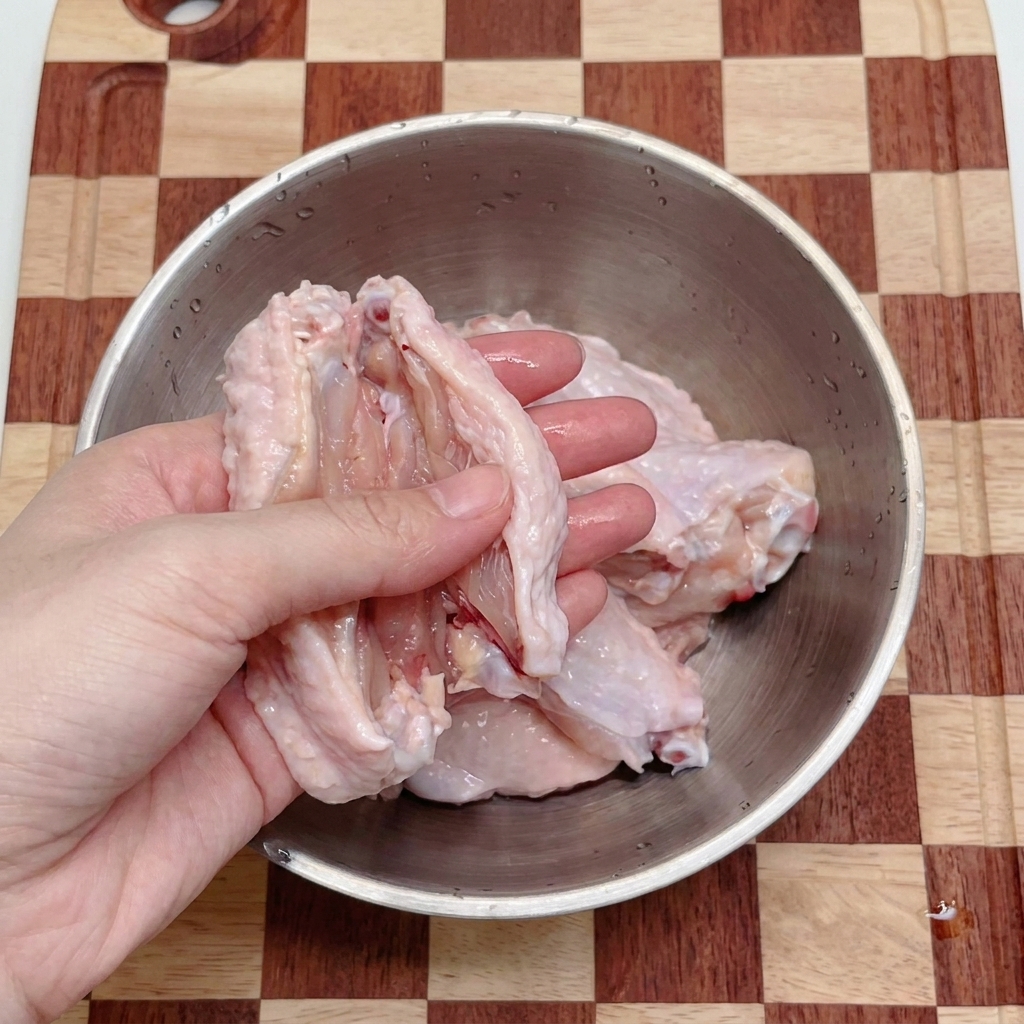 Mani che usano forbici da cucina per dividere le alette di pollo in una ciotola dacciaio.