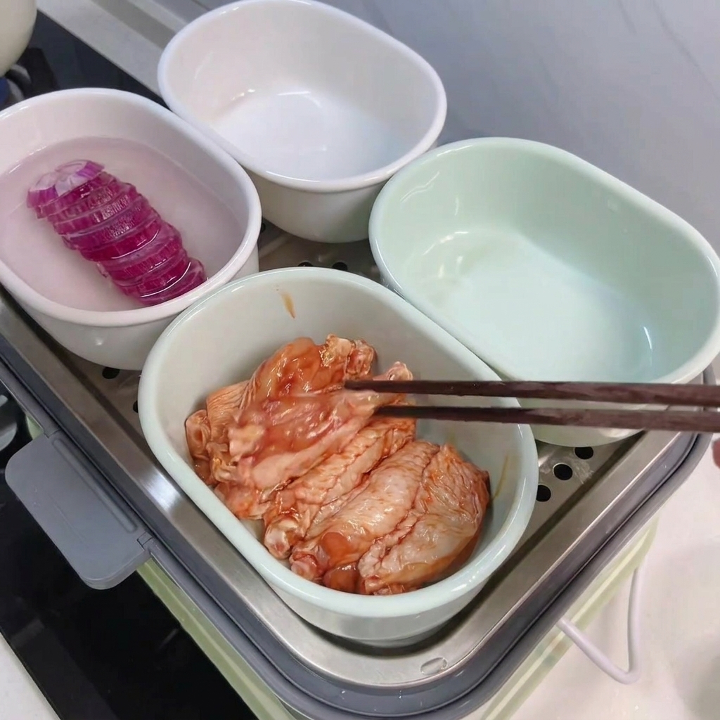 Alette marinate disposte con le bacchette in una ciotola accanto a quella del riso.