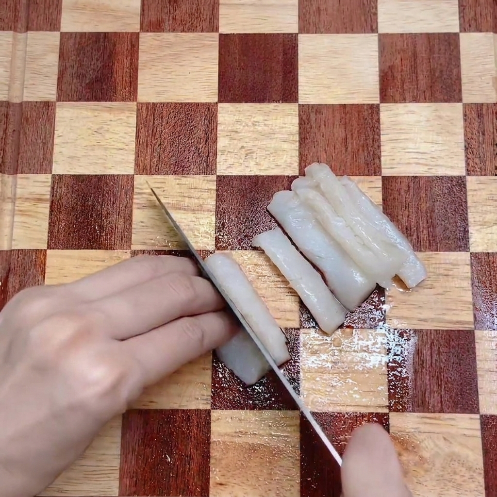 Coltello da cucina che affetta un filetto di merluzzo bianco su un tagliere di legno.
