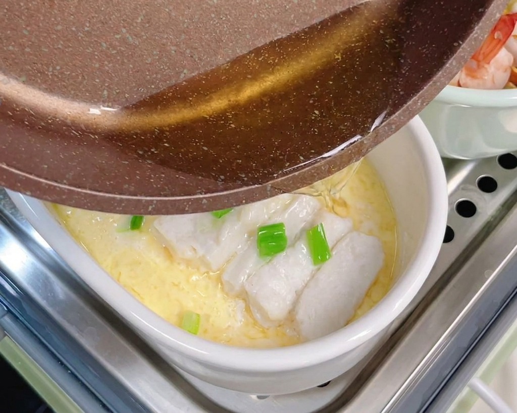 Olio bollente versato da un padellino su cipollotti e merluzzo sopra la crema duova.