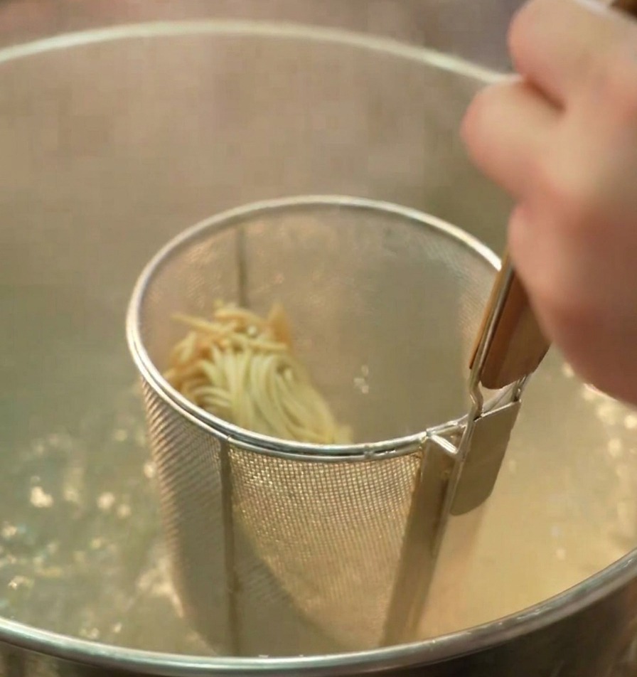 Un colino con i noodles per ramen immerso in una pentola profonda con acqua bollente.