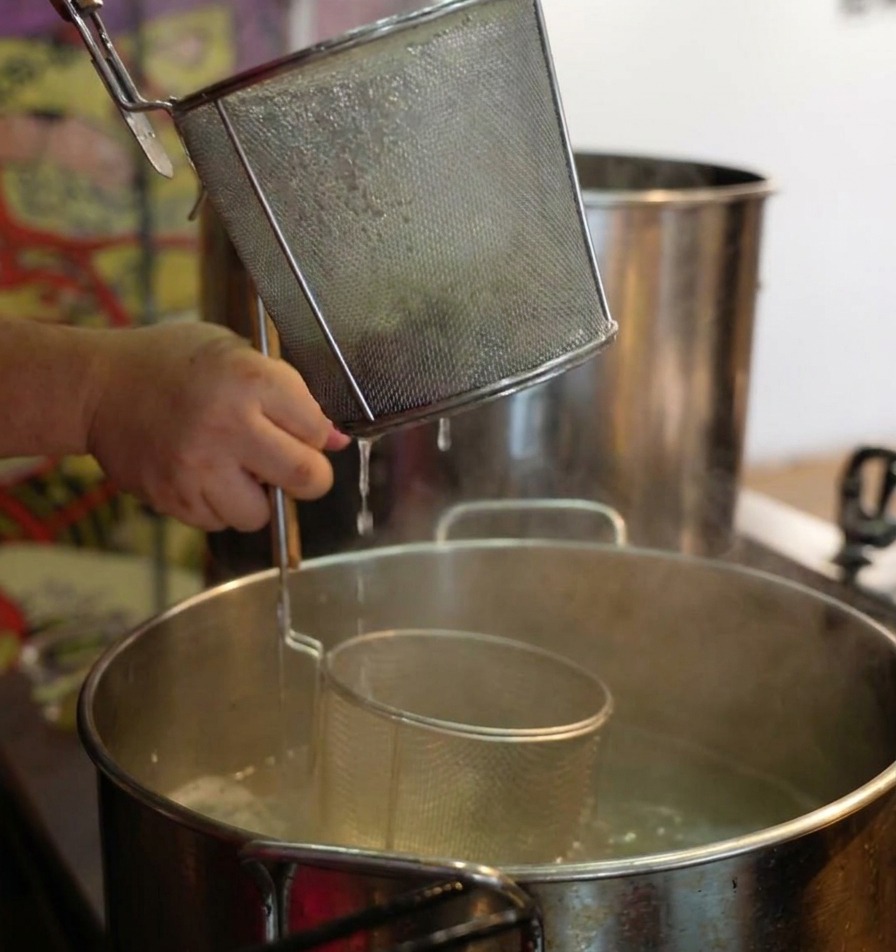 Mani che scuotono energicamente un colino a rete sopra una pentola fumante per scolare i noodles.