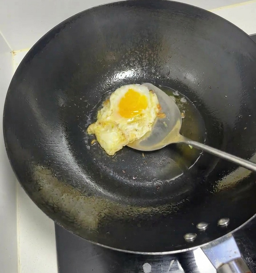 Un uovo che frigge in un wok nero ben caldo usando una spatola metallica.