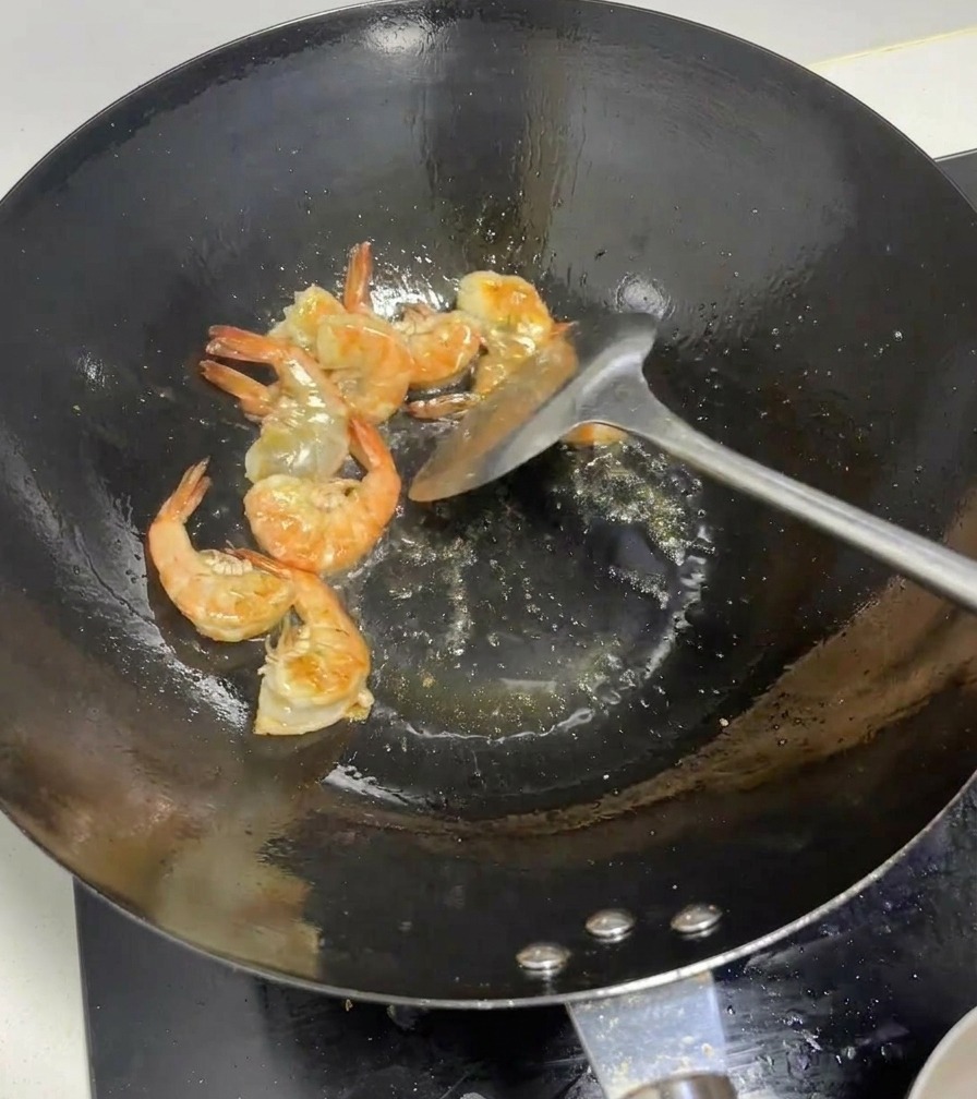 Gamberi interi che diventano di un rosa acceso mentre vengono saltati in un wok caldo.